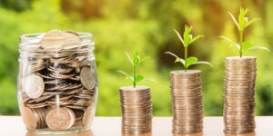 jar of coins next to stacks of coins with plants growing out of them